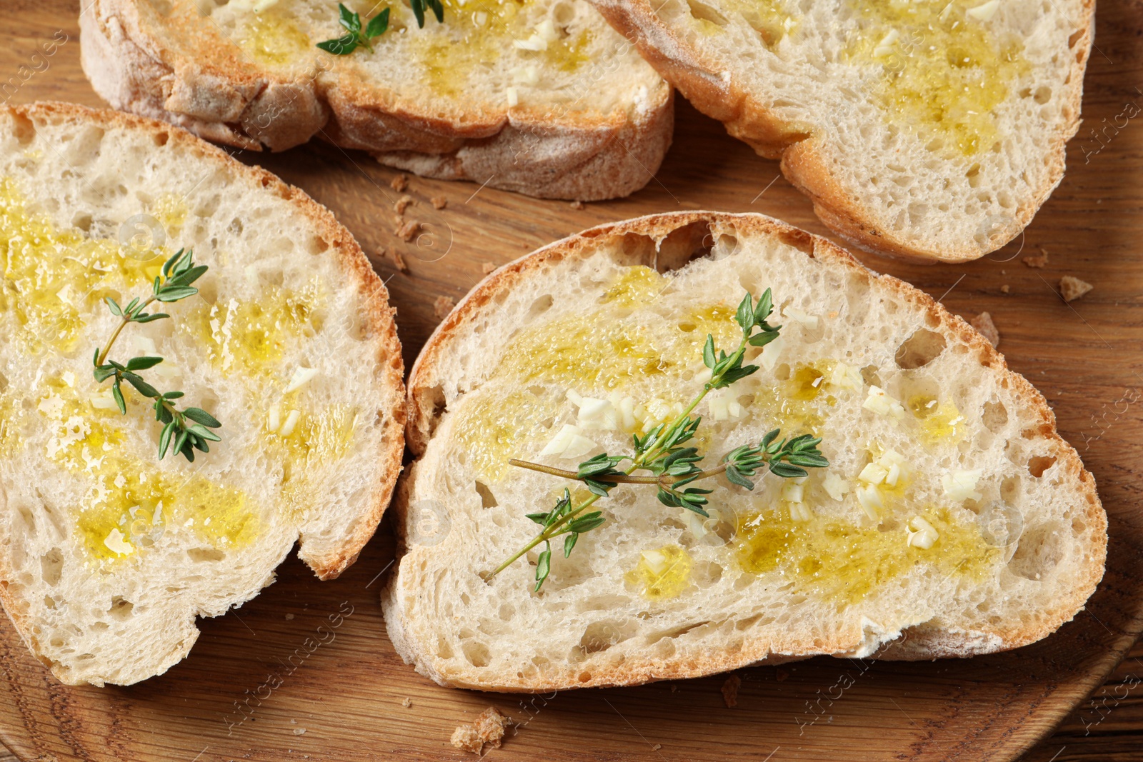 Photo of Tasty bruschettas with oil and thyme on wooden plate, top view