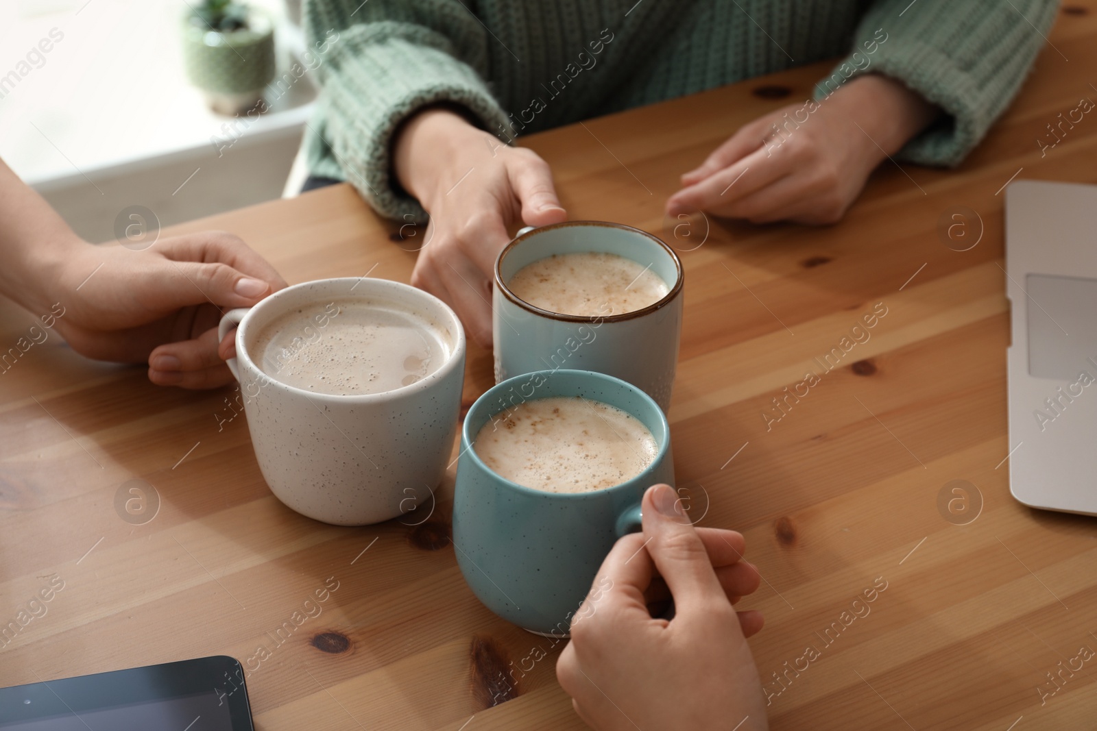 Photo of Women with cups of coffee at table in cafe, closeup