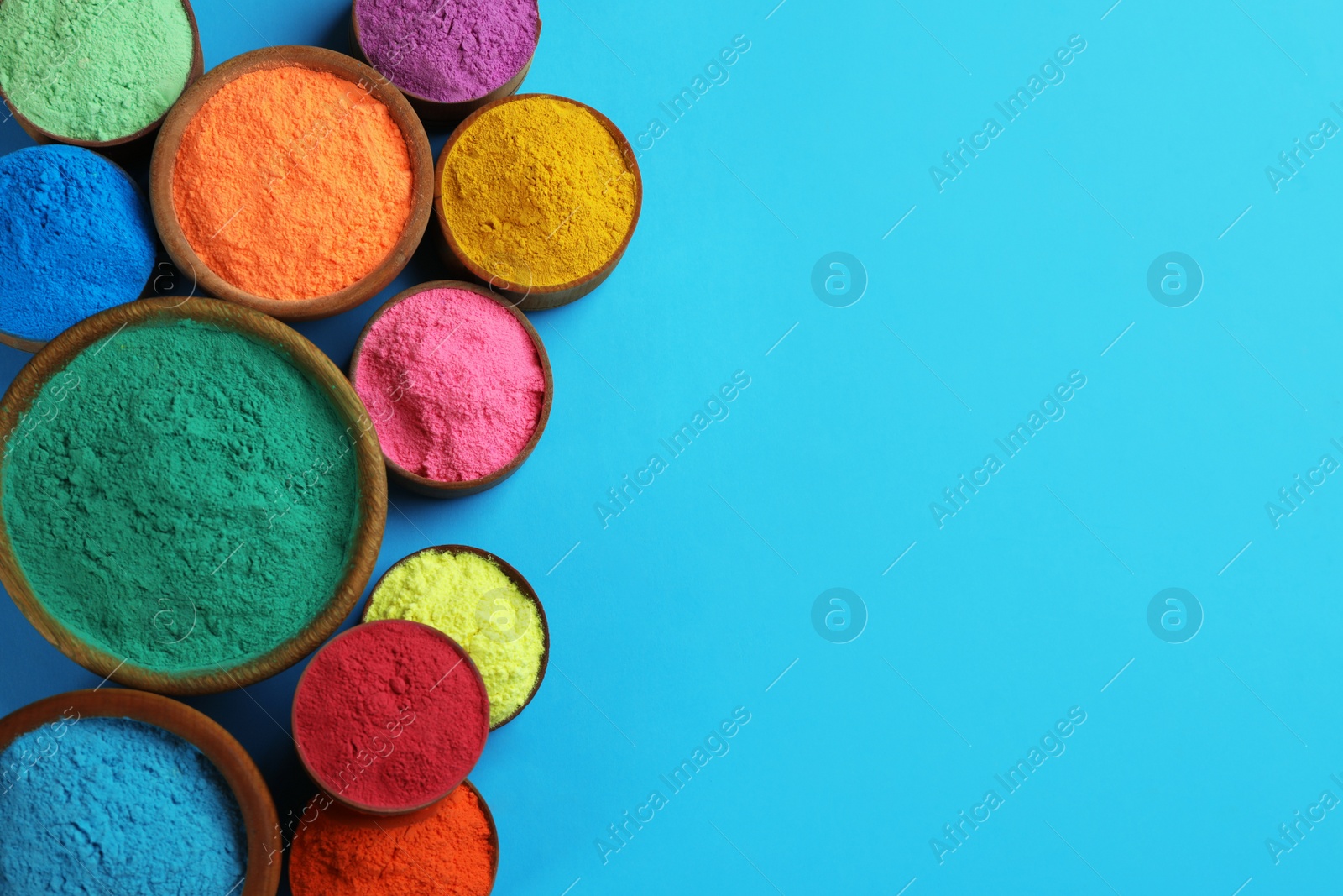 Photo of Colorful powders in bowls on light blue background, flat lay with space for text. Holi festival celebration