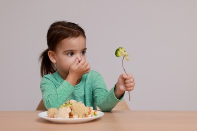 Photo of Cute little girl closing nose and refusing to eat vegetable salad at table on grey background