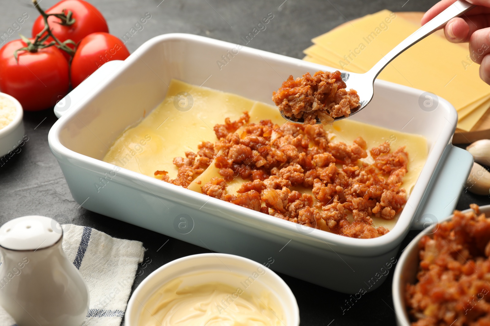 Photo of Woman making lasagna at dark table, closeup