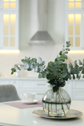 Photo of Beautiful eucalyptus branches on white table in kitchen, space for text. Interior element