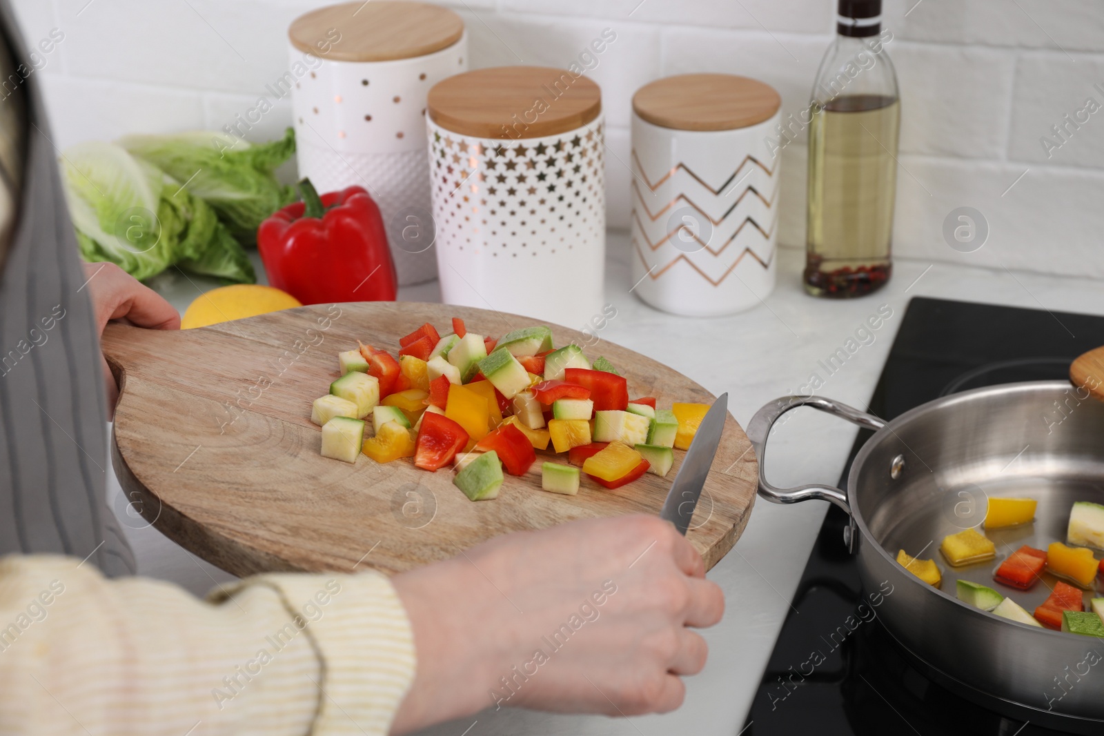 Photo of Woman putting cut vegetables into saute pan in kitchen, closeup