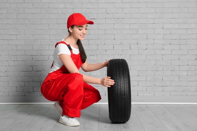 Photo of Female mechanic in uniform with car tire against brick wall background