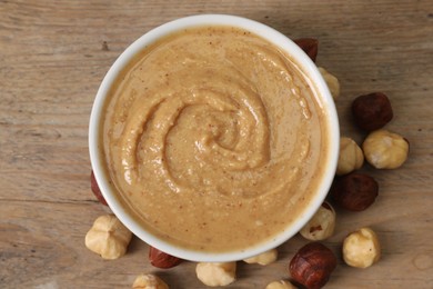 Photo of Delicious nut butter in bowl and hazelnuts on wooden table, top view