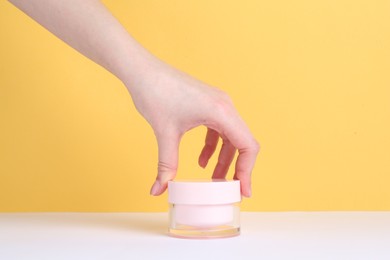 Woman with jar of cream on yellow background, closeup