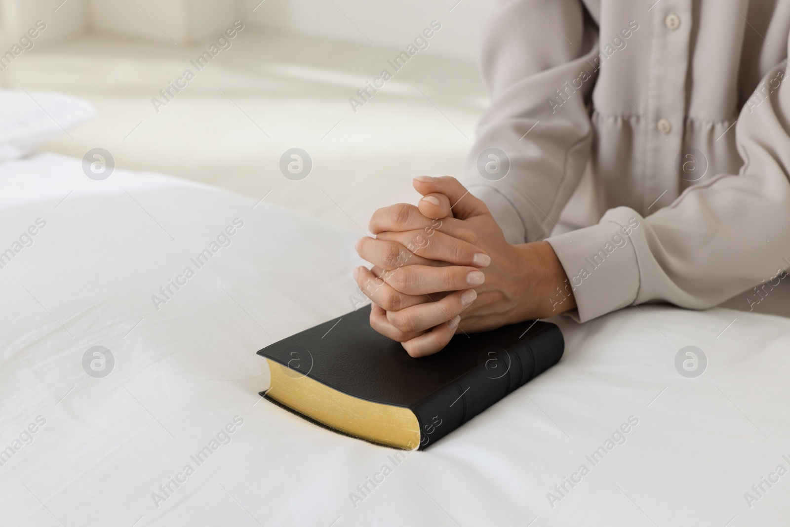 Photo of Religious woman with Bible praying in bedroom, closeup