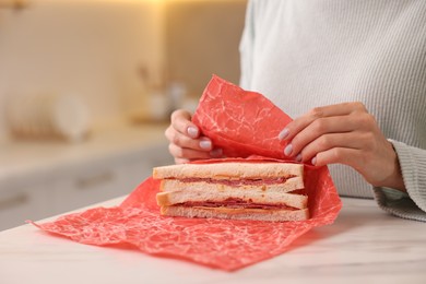 Woman packing sandwich into beeswax food wrap at light table in kitchen, closeup. Space for text