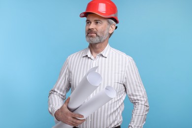 Photo of Architect in hard hat holding drafts on light blue background