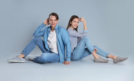 Young couple in stylish jeans sitting on grey background
