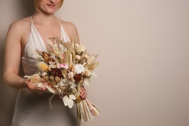 Photo of Bride holding beautiful dried flower bouquet on beige background, closeup. Space for text