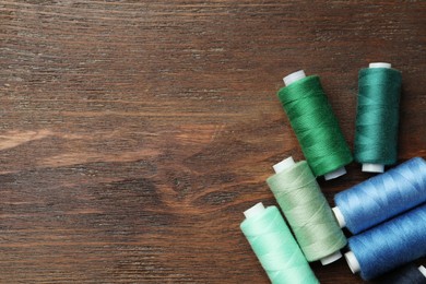 Photo of Different colorful sewing threads on wooden table, flat lay. Space for text