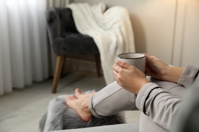 Woman with cup of hot drink resting at home, closeup. Space for text