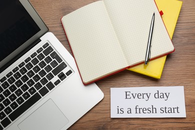 Photo of Note with motivational quote Every day is a fresh start, modern laptop and office stationery on wooden table, flat lay