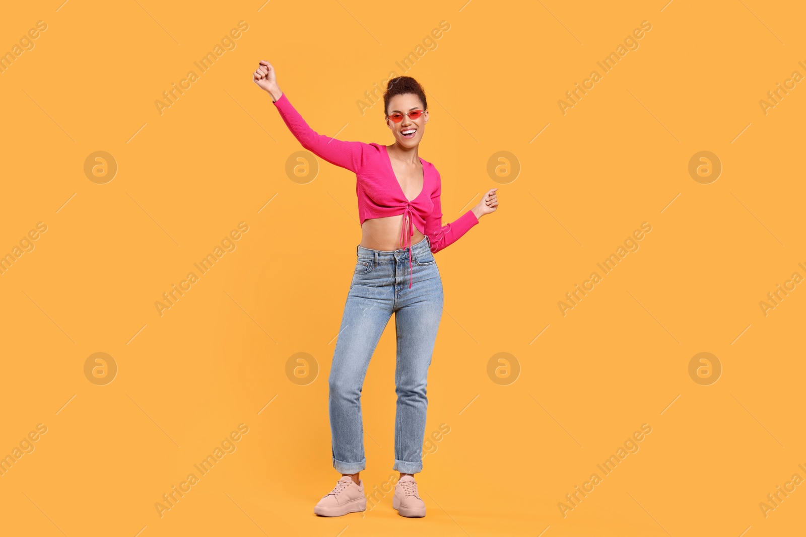 Photo of Happy young woman in stylish sunglasses dancing on orange background