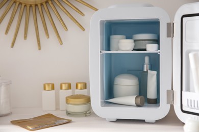 Photo of Cosmetics refrigerator and skin care products on white vanity table indoors