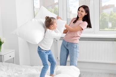 Photo of Little girl with her mother having pillow fight on bed at home