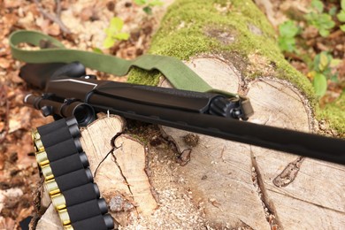 Hunting rifle and cartridges on tree stump outdoors, closeup