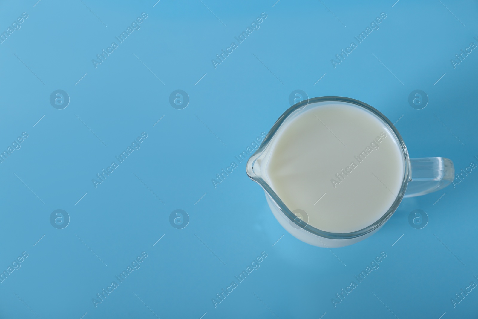 Photo of Jug of fresh milk on light blue background, top view. Space for text