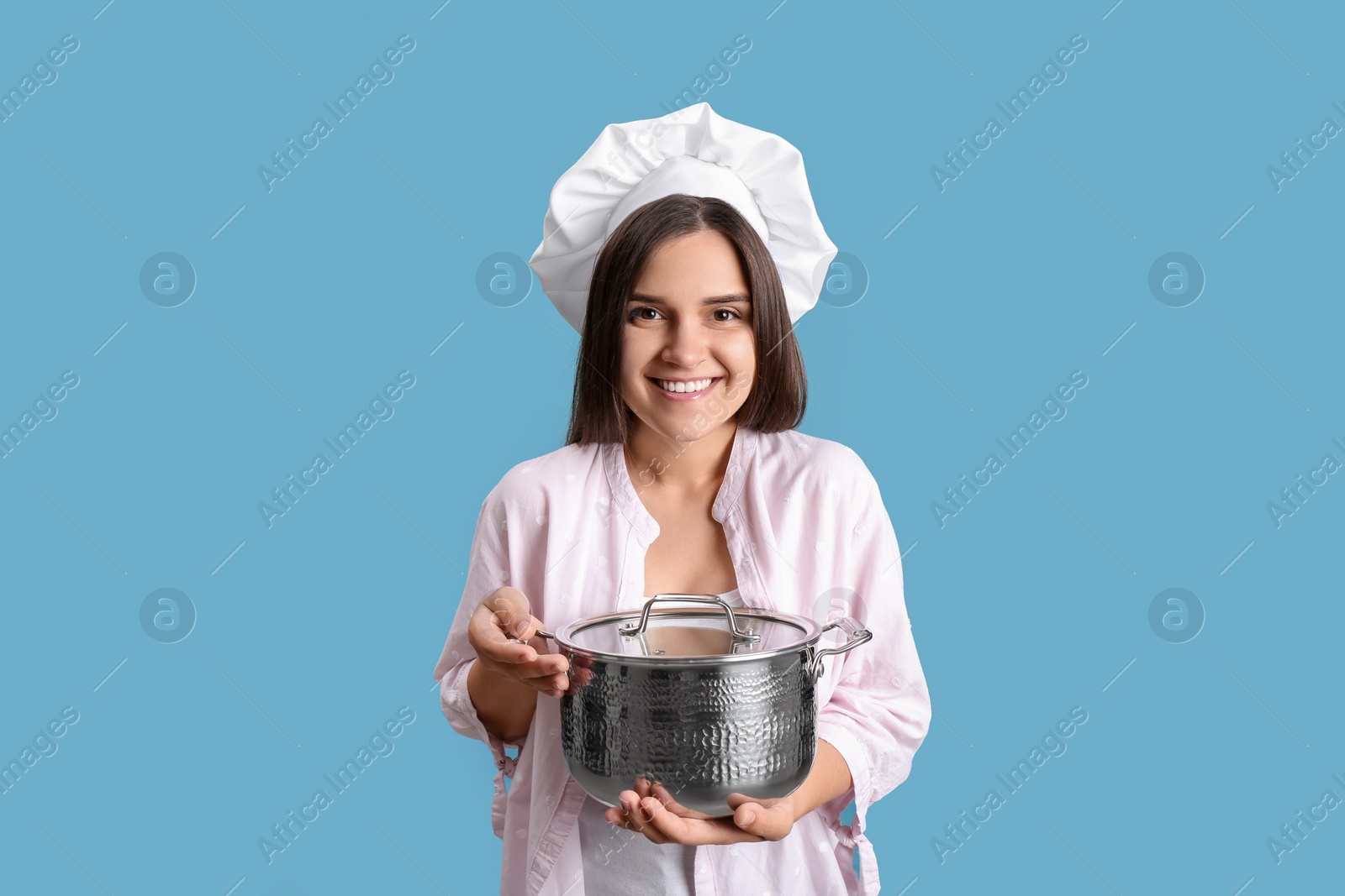 Photo of Happy young woman with cooking pot on light blue background