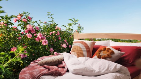 Image of Comfortable bed with soft pillows in garden with beautiful roses on sunny day