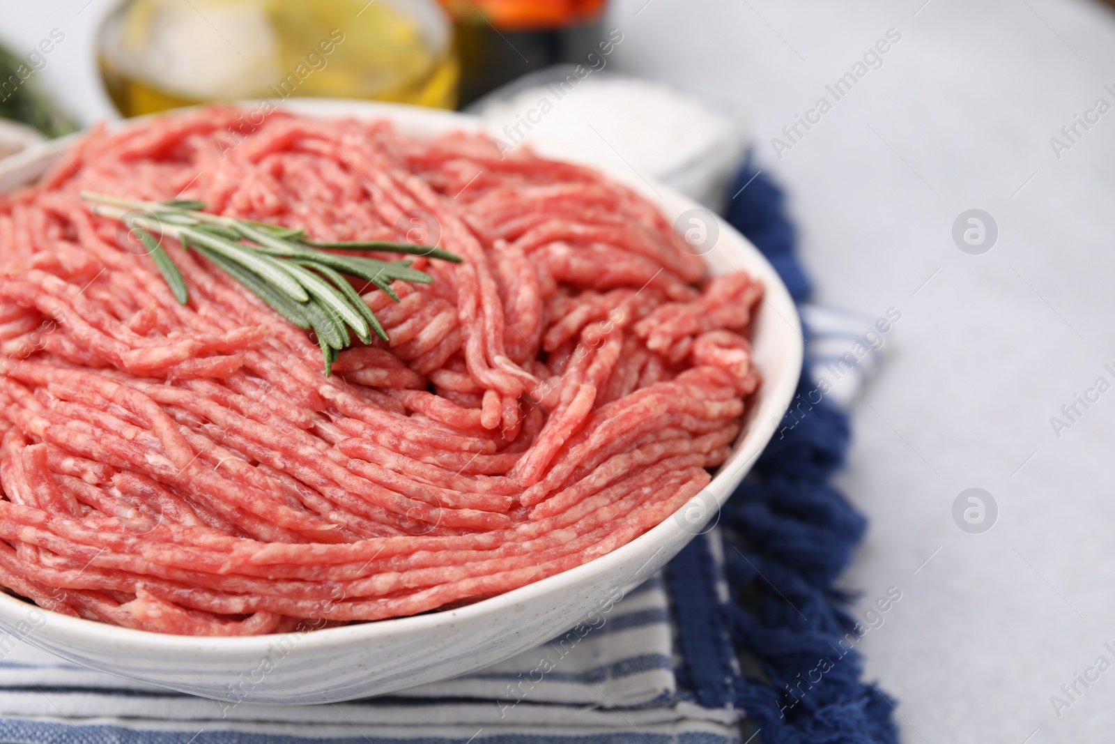 Photo of Fresh raw ground meat and rosemary in bowl on light table, closeup