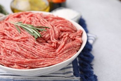 Photo of Fresh raw ground meat and rosemary in bowl on light table, closeup