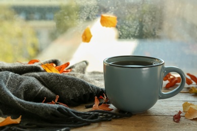 Photo of Cup of hot drink and autumn leaves near window on rainy day. Cozy atmosphere