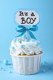 Photo of Beautifully decorated baby shower cupcake with cream and boy topper on light blue background