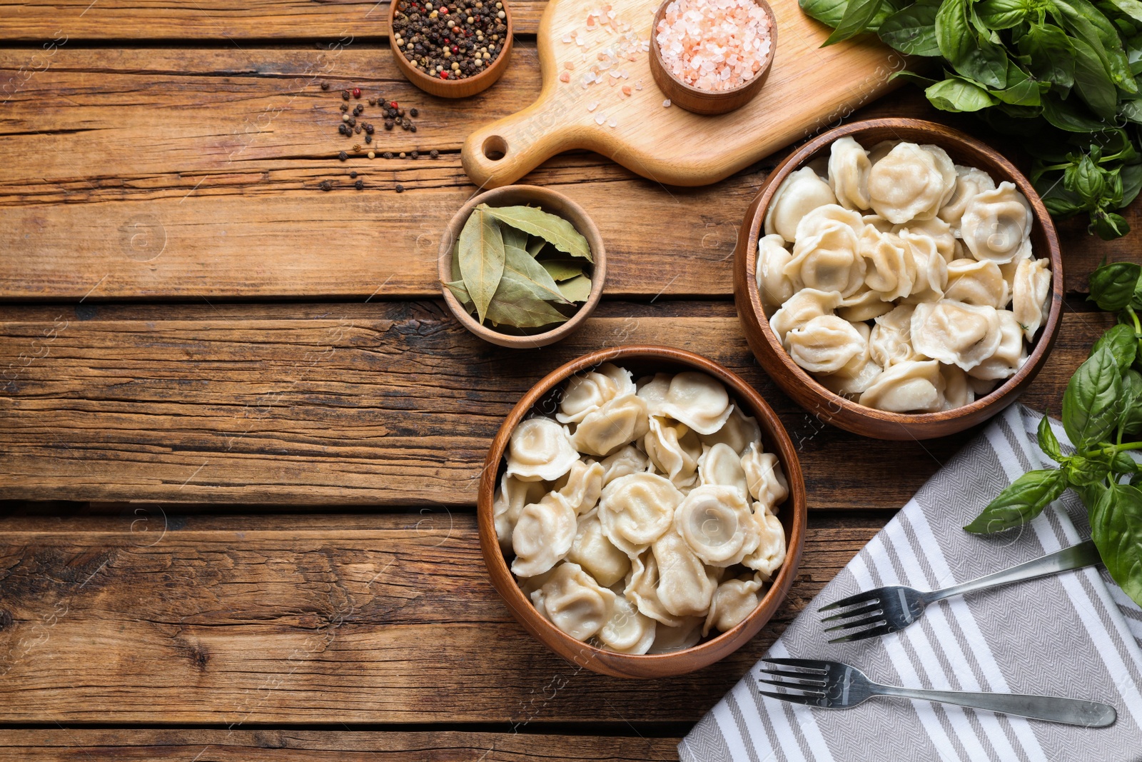 Photo of Tasty dumplings in bowls served on wooden table, flat lay. Space for text