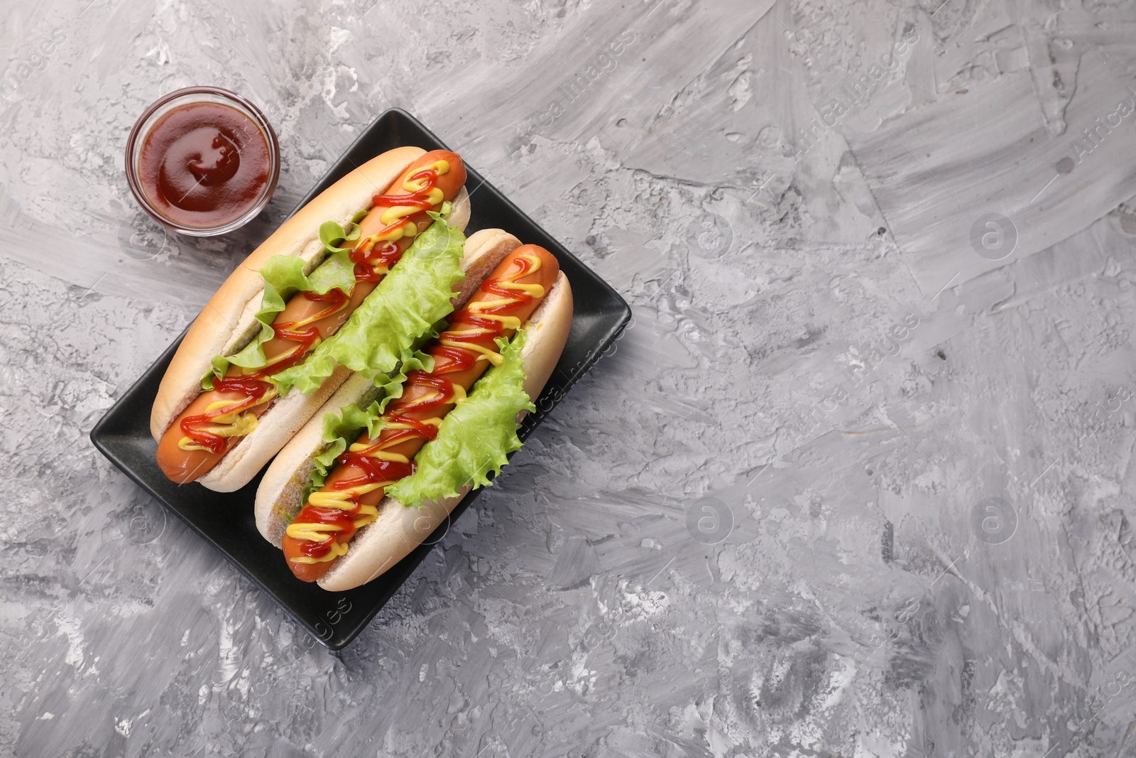 Photo of Tasty hot dogs with lettuce, ketchup and mustard on grey textured table, flat lay. Space for text