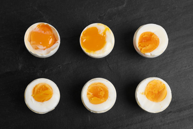 Photo of Different readiness stages of boiled chicken eggs on black table, flat lay
