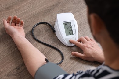 Photo of Man measuring blood pressure at wooden table, closeup