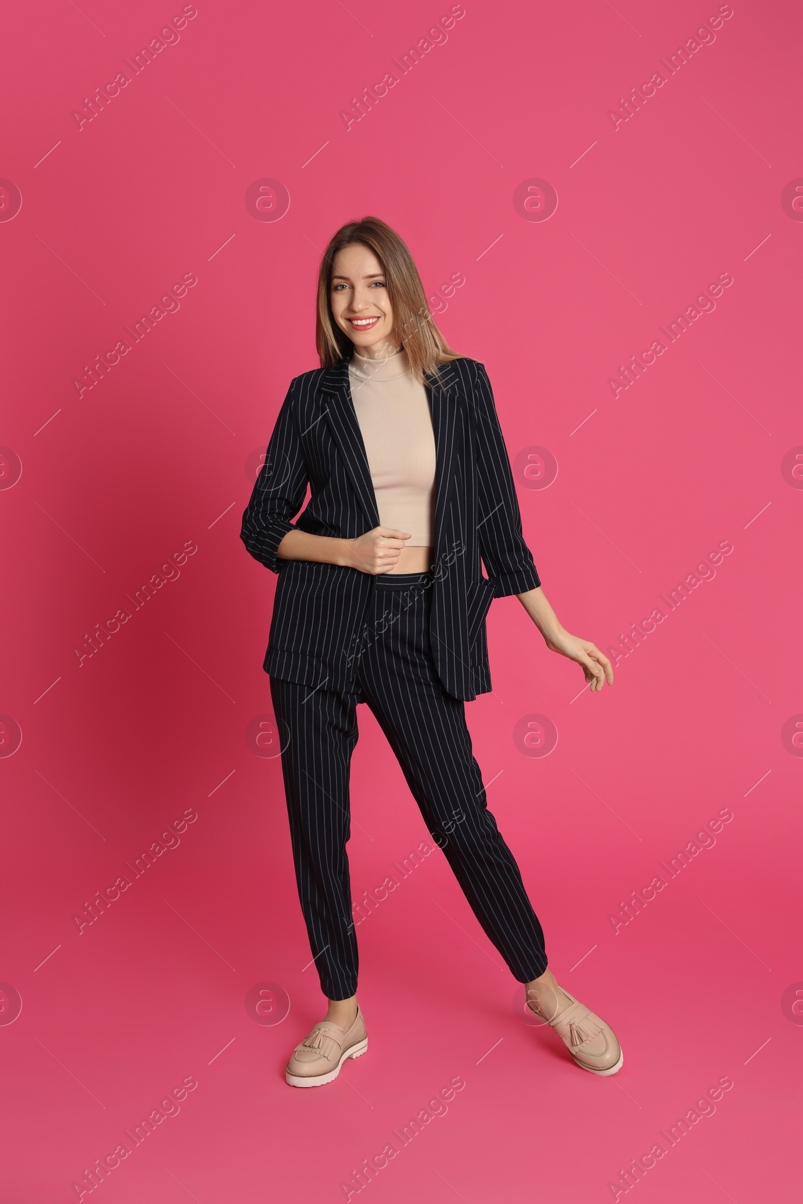 Photo of Full length portrait of beautiful young woman in fashionable suit on pink background. Business attire