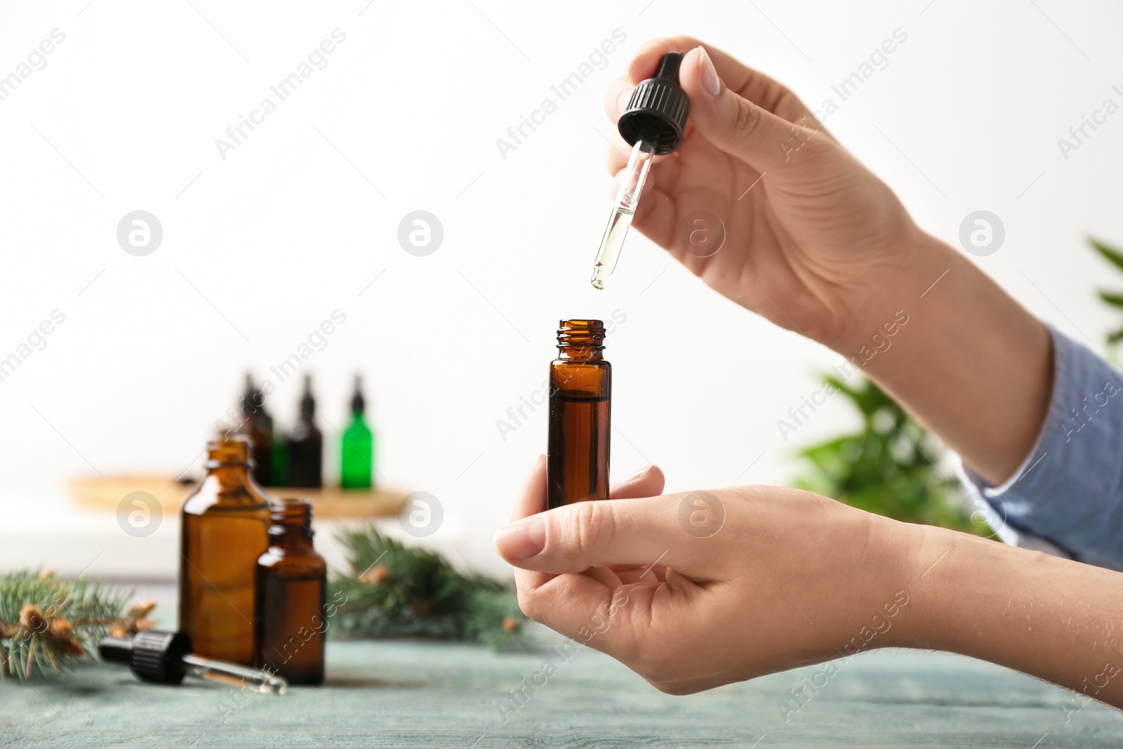 Photo of Woman dripping essential oil into glass bottle  at table, closeup