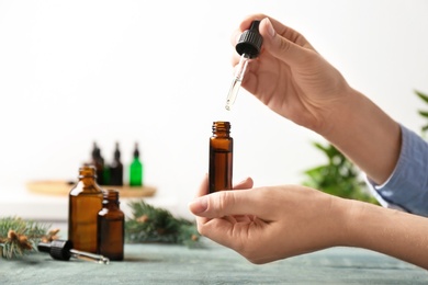 Woman dripping essential oil into glass bottle  at table, closeup