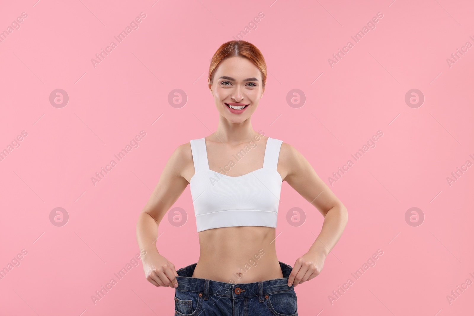 Photo of Slim woman wearing big jeans on pink background. Weight loss