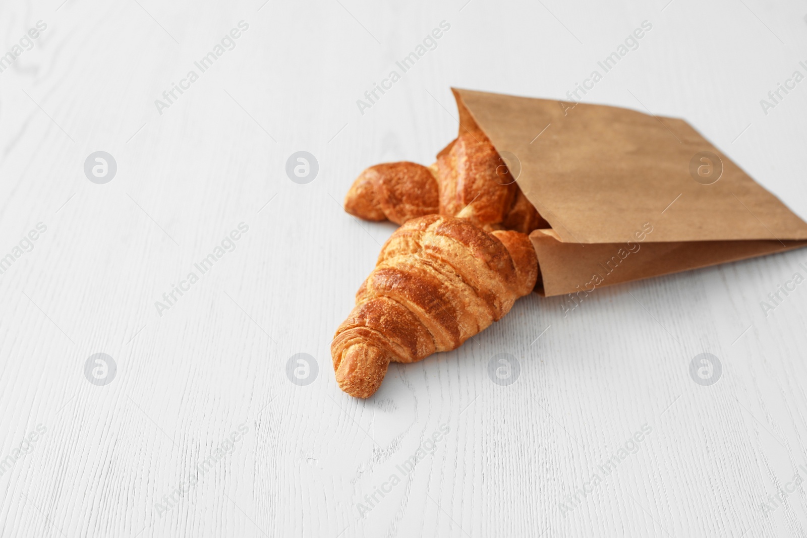 Photo of Paper bag with pastry on light wooden background. Space for text