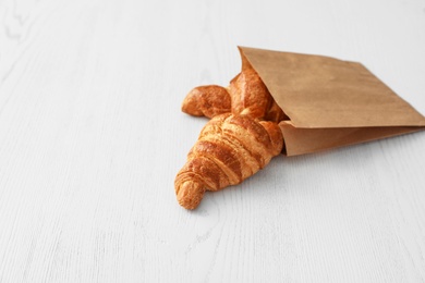 Paper bag with pastry on light wooden background. Space for text