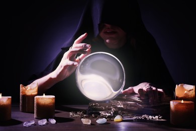 Photo of Soothsayer using crystal ball to predict future at table in darkness. Fortune telling