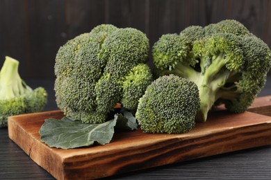 Board with fresh raw broccoli on black wooden table, closeup