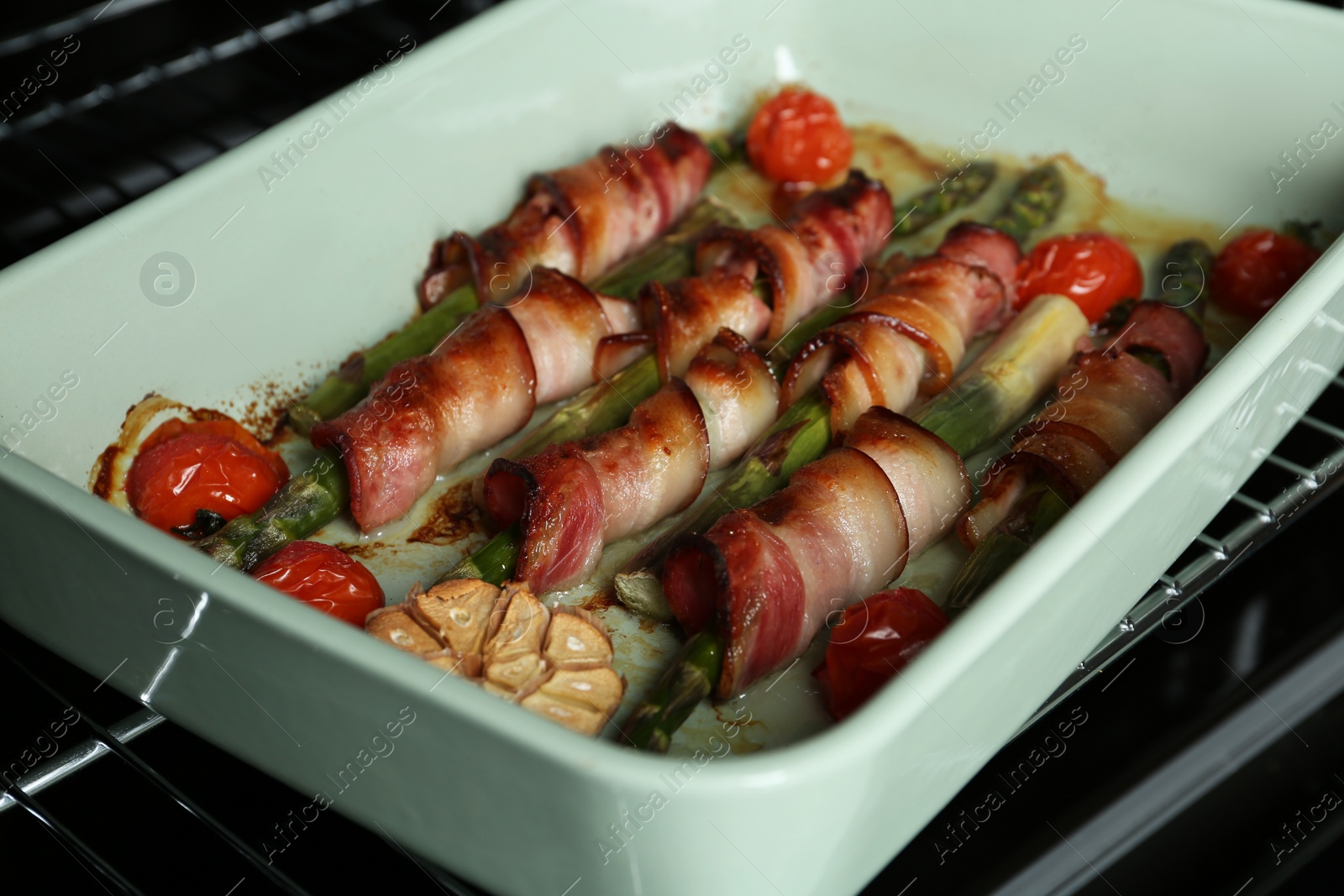 Photo of Bacon wrapped asparagus in baking dish on oven rack, closeup