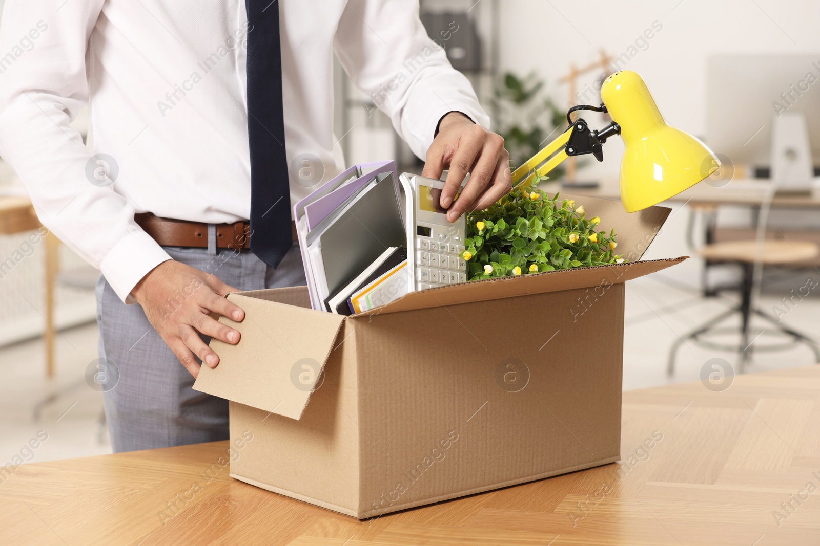 Photo of Unemployment problem. Man with box of personal belongings at table in office, closeup