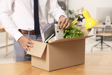 Photo of Unemployment problem. Man with box of personal belongings at table in office, closeup