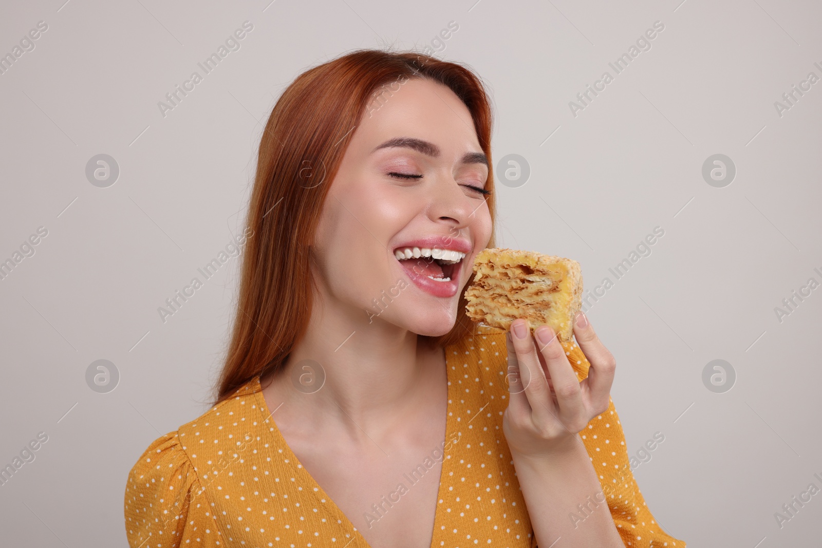 Photo of Young woman eating piece of tasty cake on light grey background