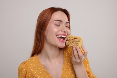 Young woman eating piece of tasty cake on light grey background