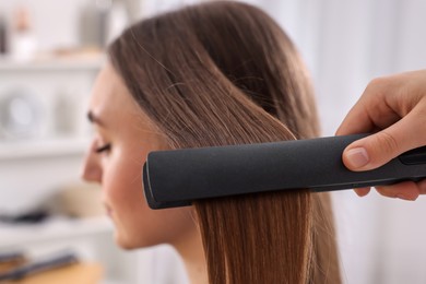 Photo of Hairdresser straightening woman's hair with flat iron in salon, selective focus