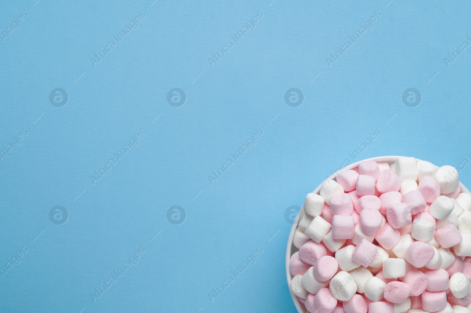 Photo of Bowl with delicious marshmallows on light blue background, top view. Space for text