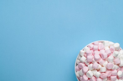 Photo of Bowl with delicious marshmallows on light blue background, top view. Space for text