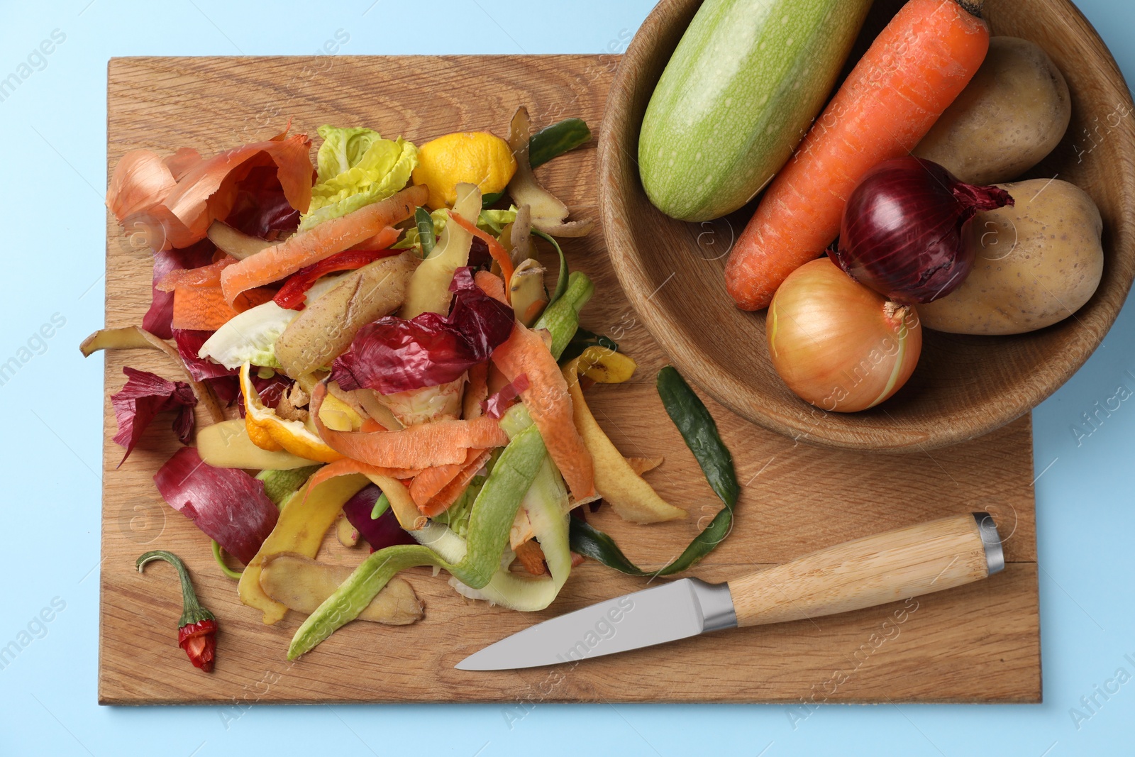 Photo of Different fresh vegetables with peels and knife on light blue background, top view